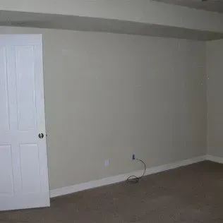 Interior of a room with a white door, beige walls, and brown carpet.