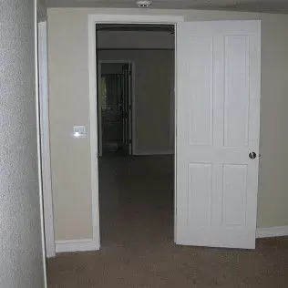 White door open to a room with carpet and a doorway to another room. A light switch is on the wall.