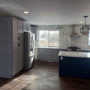Kitchen with gray cabinets, stainless steel appliances, blue island, and brick backsplash.
