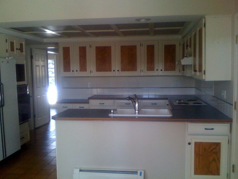 Kitchen with white cabinets, wood accents, dark countertops, sink, and cooktop.