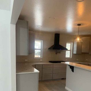 Kitchen with gray cabinets, a black range hood, and a hanging light.
