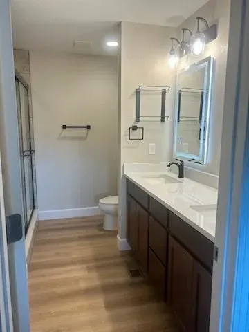 Bathroom with light wood floor, white countertop, dark brown cabinets, and a glass shower.