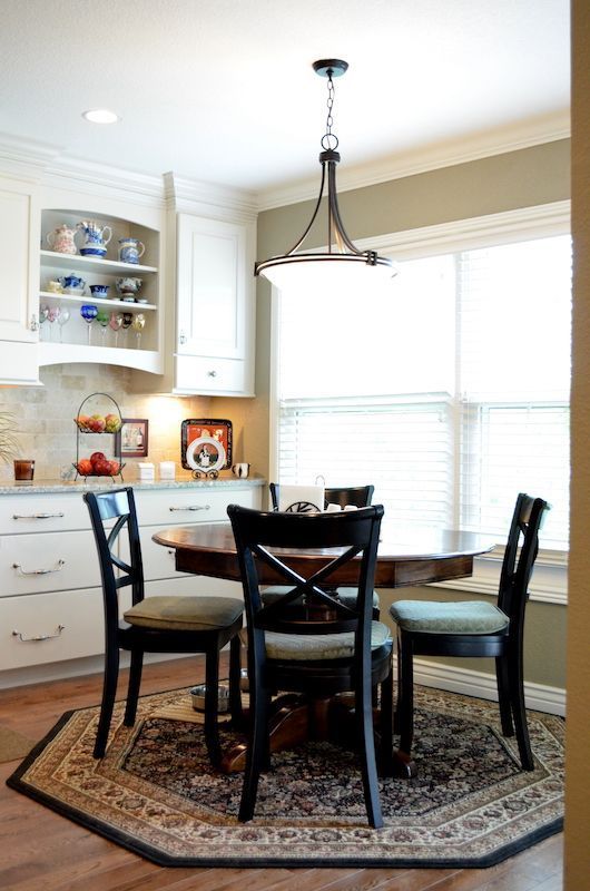 Kitchen with round table, black chairs, and rug, under a pendant light.
