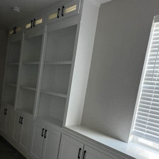 White built-in bookshelves with cabinet doors and a window with closed blinds.