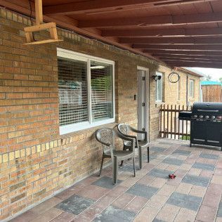 Brick patio with chairs, a grill, and a window under a covered porch.