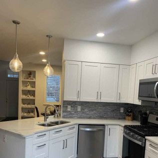 White kitchen with island, cabinets, stainless steel appliances, and two pendant lights.
