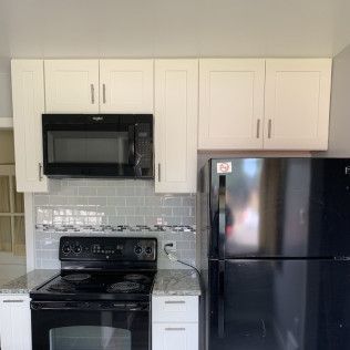 Kitchen with cream cabinets, black appliances, gray backsplash, and a black refrigerator.