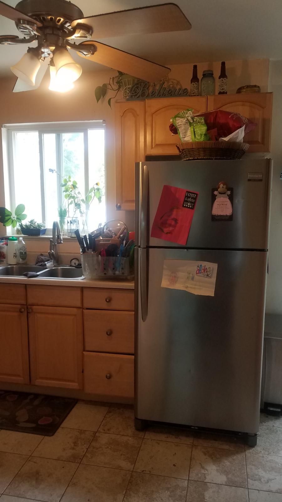 Kitchen with wooden cabinets, stainless steel refrigerator, and a window.