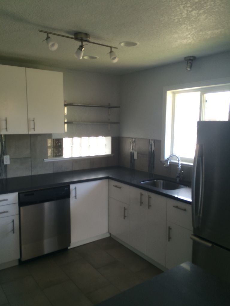 Kitchen with white cabinets, stainless steel appliances, dark countertops, and a window.