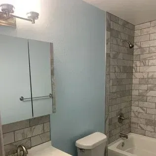 Bathroom with pale blue wall, gray tiled shower and vanity backsplash, and white toilet.
