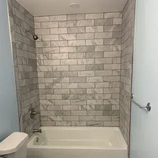 Bathroom with white tub, gray tile shower walls, and light blue wall.
