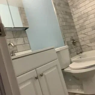 White bathroom with a white sink cabinet, toilet, and marble tile walls.