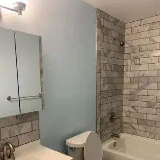 Bathroom with gray tiled shower, toilet, and light blue wall.
