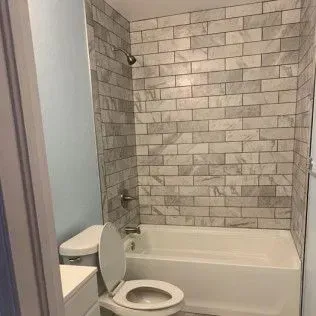 Bathroom with white tub, toilet, light blue walls, and tiled shower walls.
