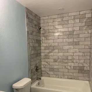 Bathroom with a tiled shower, white tub, toilet, and blue wall.