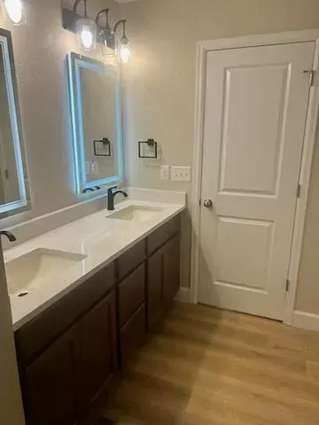 Bathroom with a double vanity, brown cabinets, white countertop, and a white door.