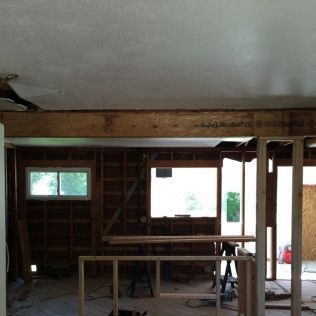 Interior view of a room under renovation. Exposed wooden beams and framing. Window and damaged ceiling visible.