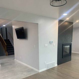 Interior view of a modern home with a mounted TV, fireplace, and staircase. Gray walls and flooring.