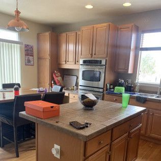 Kitchen with island, cabinets, oven, and table with chairs. Orange box and items on island.