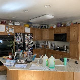 Kitchen with wooden cabinets, a central island, and appliances. Surfaces are cluttered with items.