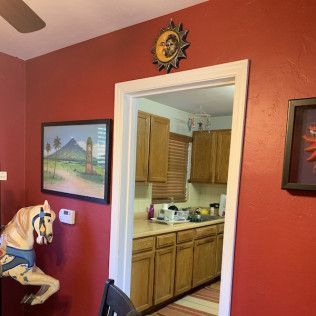 Red dining room with a doorway to a kitchen, artwork, and a carousel horse mounted on the wall.