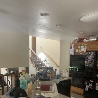 Kitchen with stairs in background, overhead lighting, cabinets, appliances, and sink.