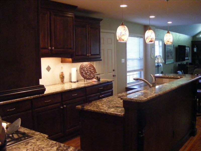Dark wood kitchen with granite countertops, pendant lights, and a door to the outside.