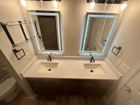 Bathroom with double sinks, two mirrors with lights, and dark brown cabinets.