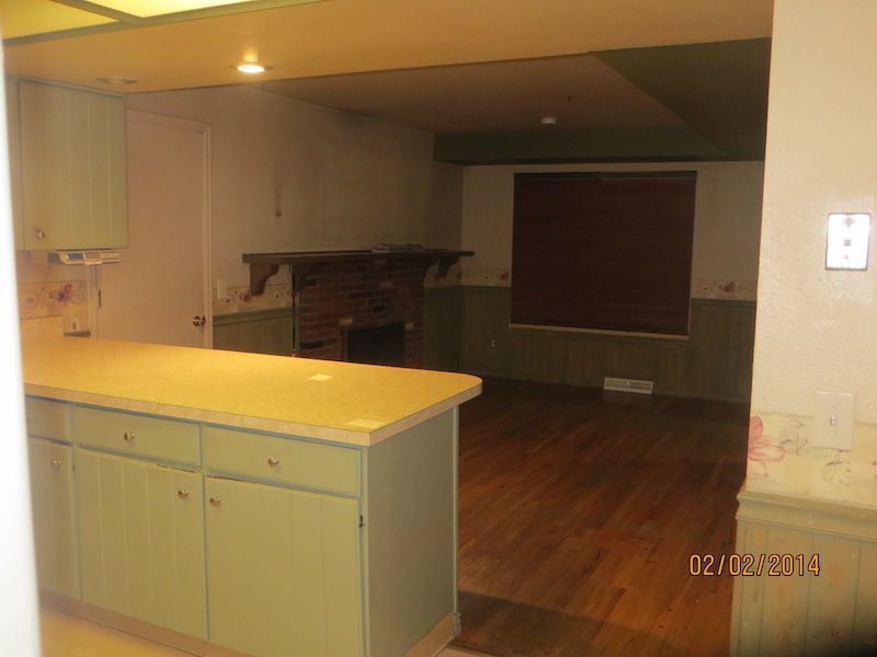 Kitchen with pale green cabinets, light wood countertop, and view into living room with a fireplace and dark wood floor.