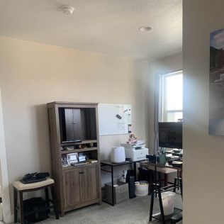 A home office with a cabinet, desk, and window. A whiteboard and printer are also visible.