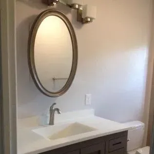 Bathroom with an oval mirror, sink, and cabinet.  A light fixture is above the mirror.