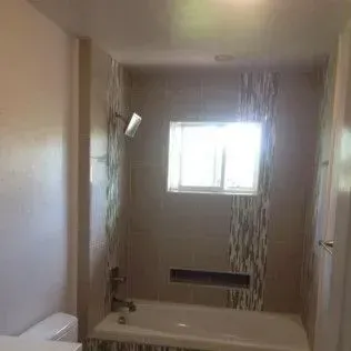 Bathroom with a shower and a bathtub, tiled walls, and a window.