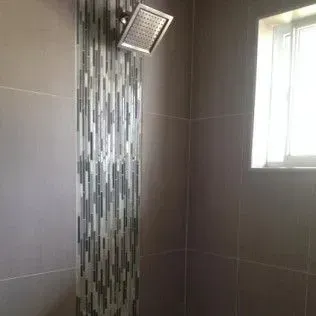 Shower with a column of mosaic tile, gray wall tiles, and a window on the right.