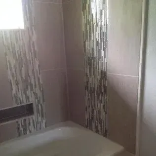 Bathroom with a tiled wall, decorative mosaic strip, and bathtub.