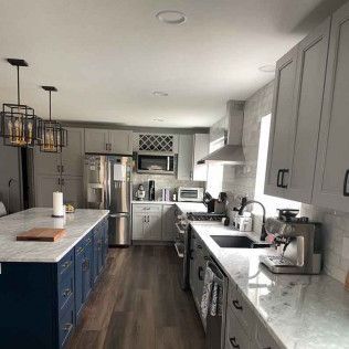 Modern kitchen with blue island and gray cabinets, stainless steel appliances, and wood flooring.