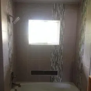 Bathroom with a tiled shower, window, and a strip of decorative tiles.