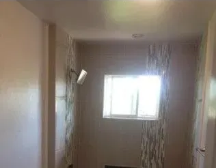 Empty bathroom with a window and a showerhead. Light-colored walls and patterned accent tile.