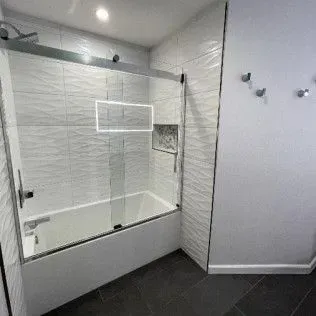 Modern bathroom with white textured tile, glass shower door, and dark gray floor.