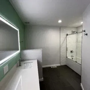 Modern bathroom with white countertops, green wall, dark floor, and shower.