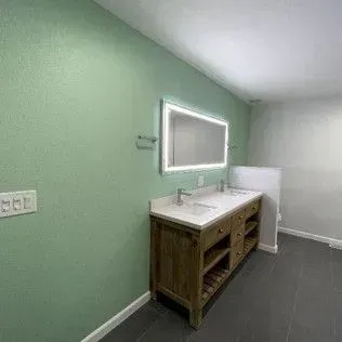 Bathroom with green walls, a wooden vanity, a lit mirror, and dark tile floor.