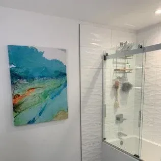 Bathroom with abstract painting on the wall, glass shower door, and white textured tile.