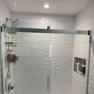 Modern bathroom shower with glass sliding door and white textured tile walls.