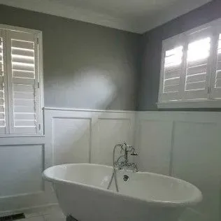 Bathroom with a white clawfoot tub, shutters, and gray walls with white wainscoting.