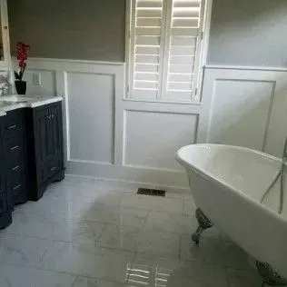 Bathroom with white marble floor, a claw-foot tub, dark cabinets, and a window with white shutters.