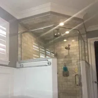 Glass shower enclosure with white trim and beige tile, built-in shelf, and chrome fixtures.
