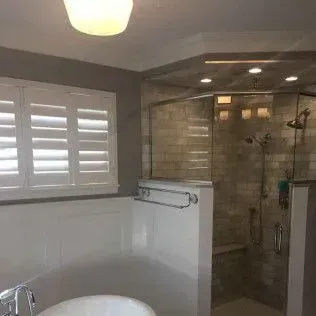 Bathroom with white shutters, a glass-enclosed shower, and a white bathtub. The walls are gray and white.