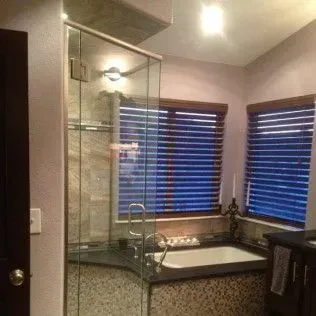 Bathroom with glass shower, wooden blinds, and a bathtub.
