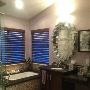 Bathroom with wood blinds, oval mirror, dark cabinets, and bathtub.