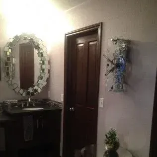 Bathroom with a dark vanity, mirror with mosaic tiles, a brown door, and art on a lilac wall.