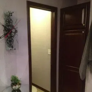 A doorway and dark wooden cabinet. A decorative clock hangs on the wall, and a plant sits on a table.
